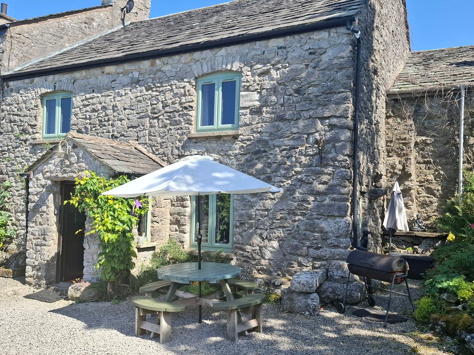 An outdoor area with a stone house, table, umbrella, and grill at The Old Farmhouse at Brackenthwaite Farm Yealand Redmayne near Arnside