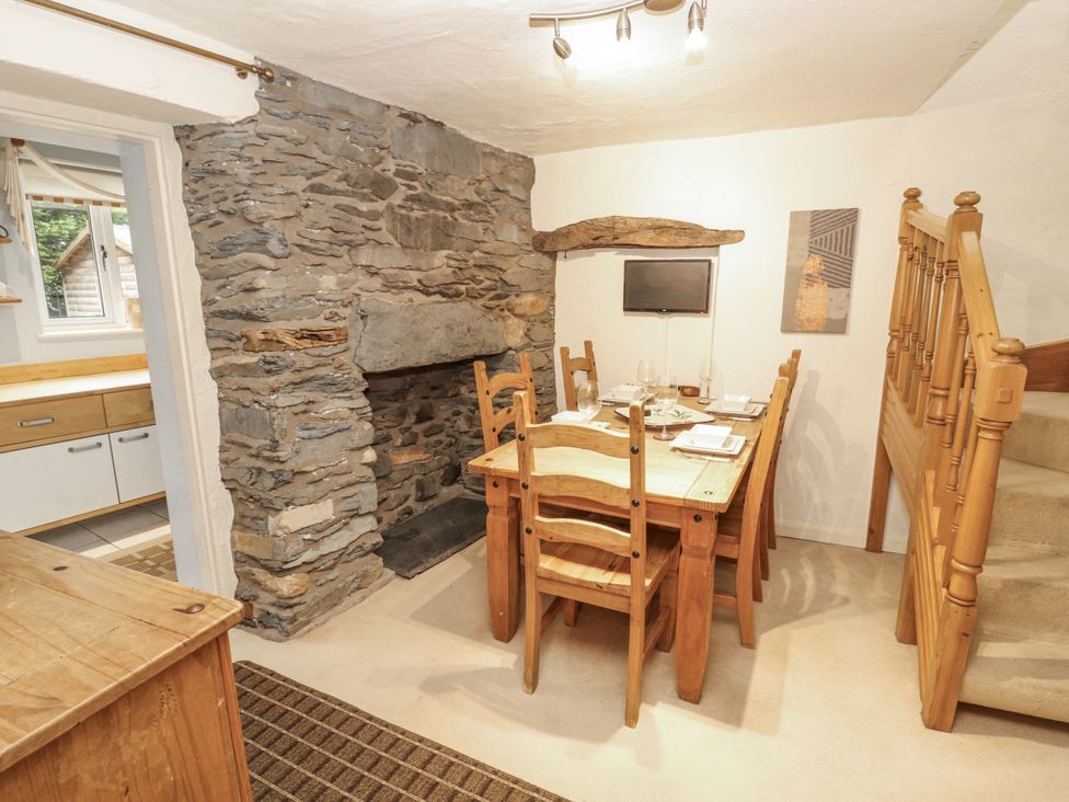 A dining room with a stone fireplace and wooden table and chairs at 2 Bens Row Backbarrow near Newby Bridge