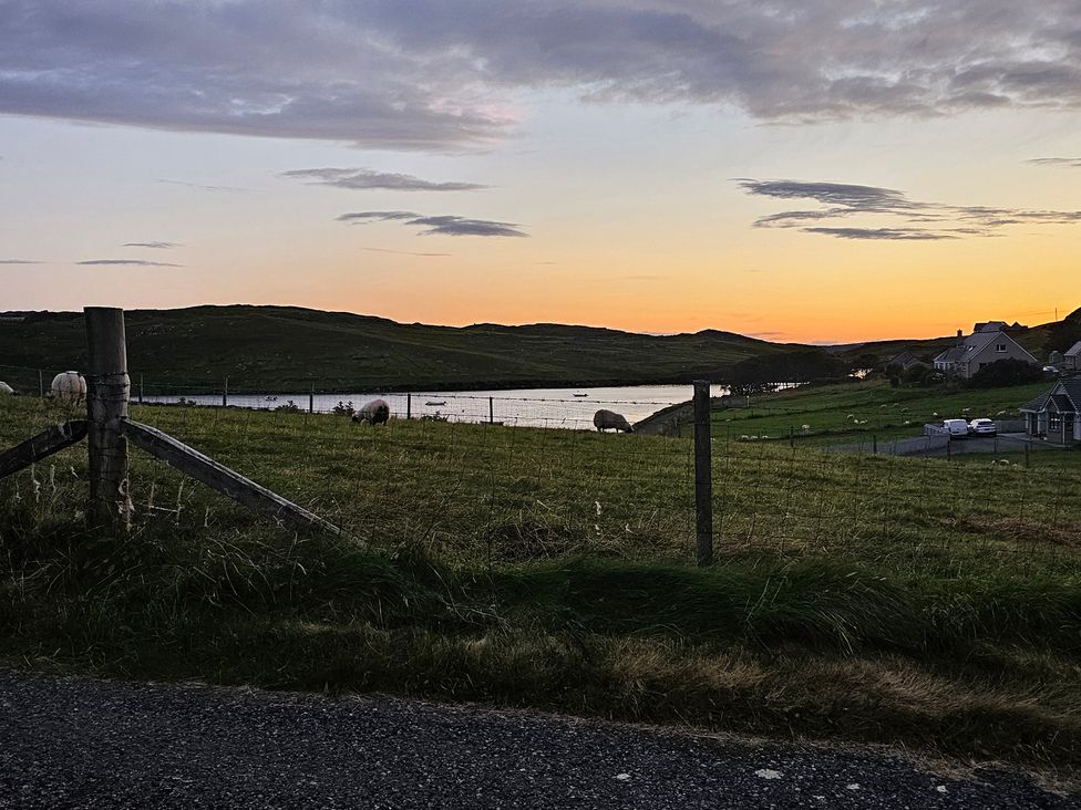 A landscape with sheep grazing and a sunset over water at 11 Knock Carloway
