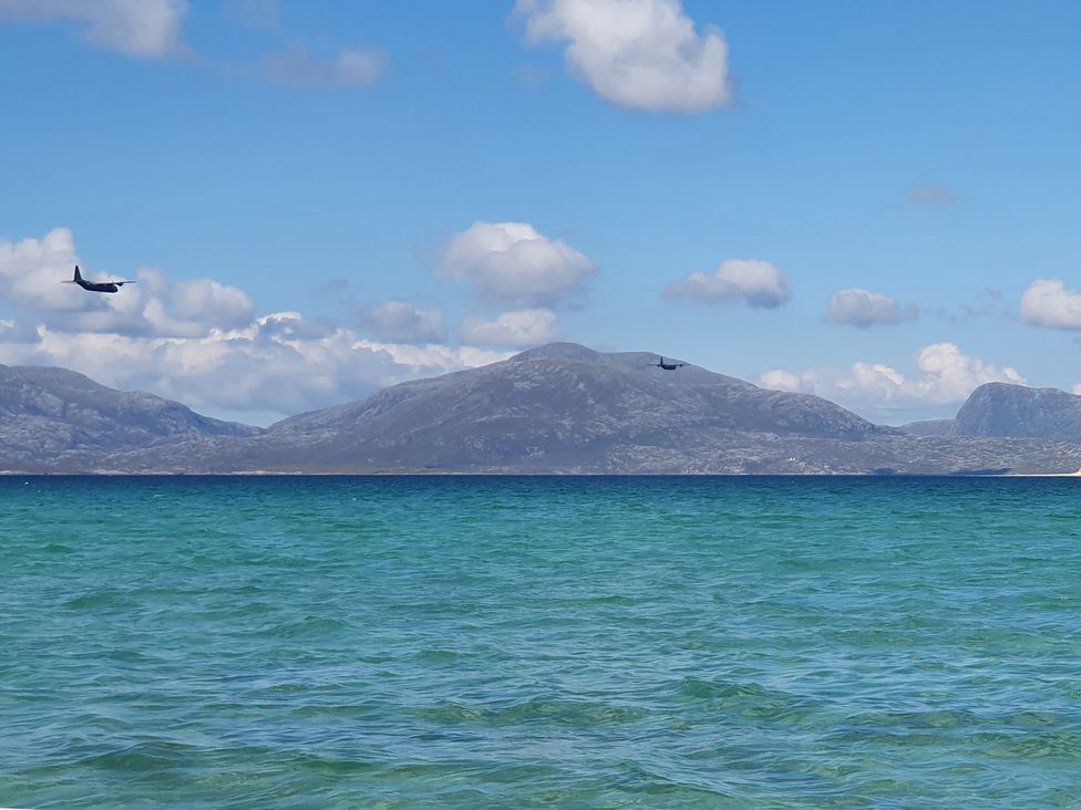 An airplane flying over the ocean with mountains in the background at 11 Knock Carloway