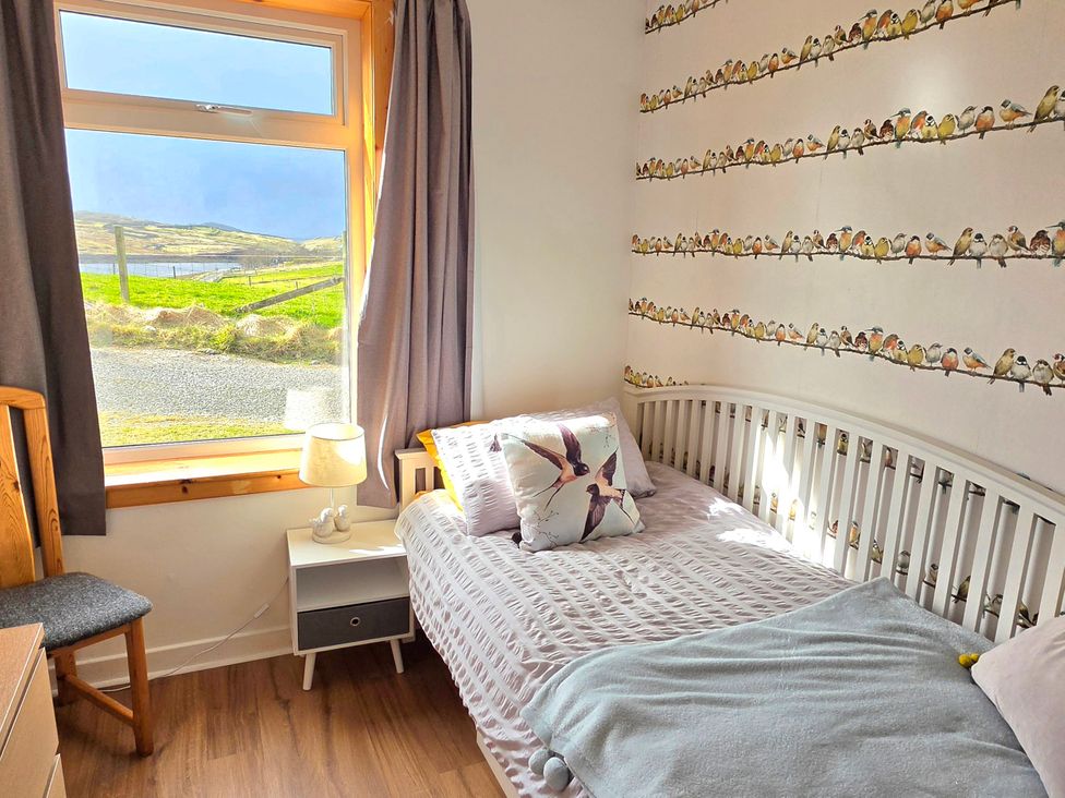 A bedroom with a single bed and a window overlooking the landscape at 11 Knock in Carloway