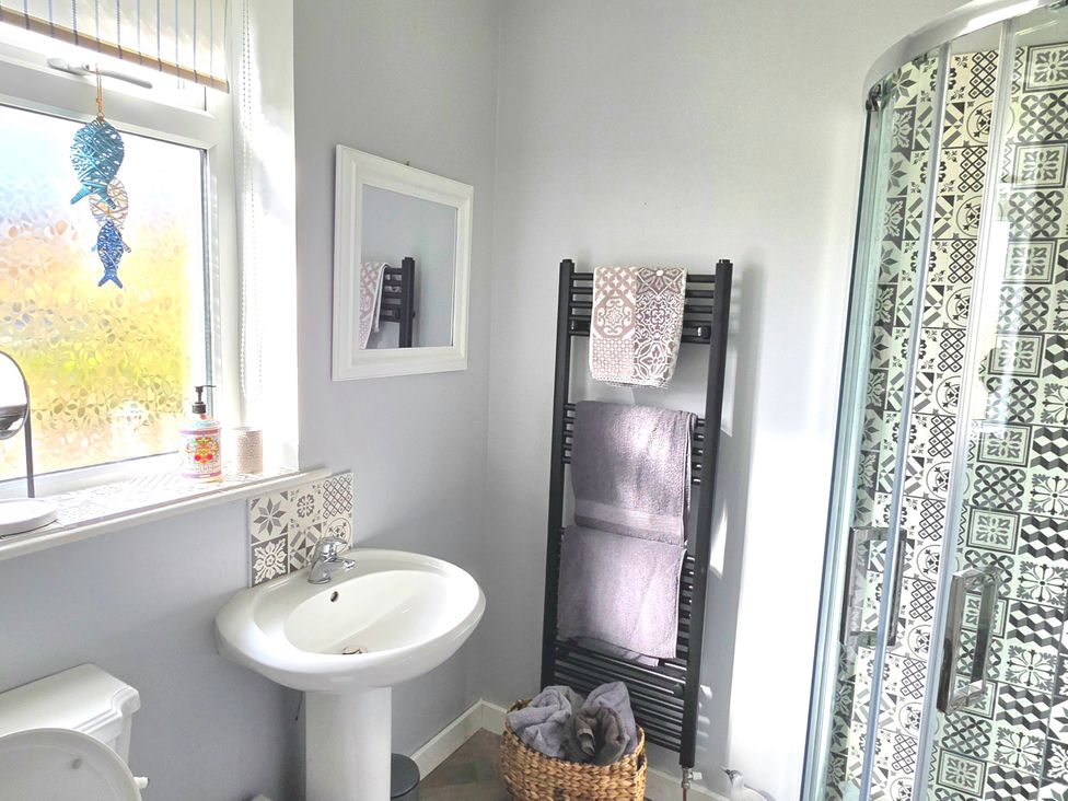 A bathroom with a sink, toilet, towel rack, and shower at 11 Knock in Carloway