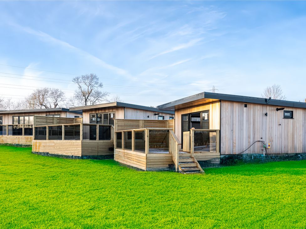 A wooden cabin with a deck and grass area at Nightingale Lodge in Yarm