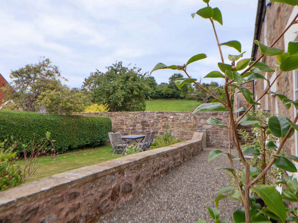 A garden with a stone wall and a table with chairs at Isfryn