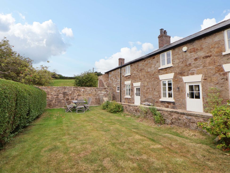 A garden with a table and chairs next to a stone house at Isfryn