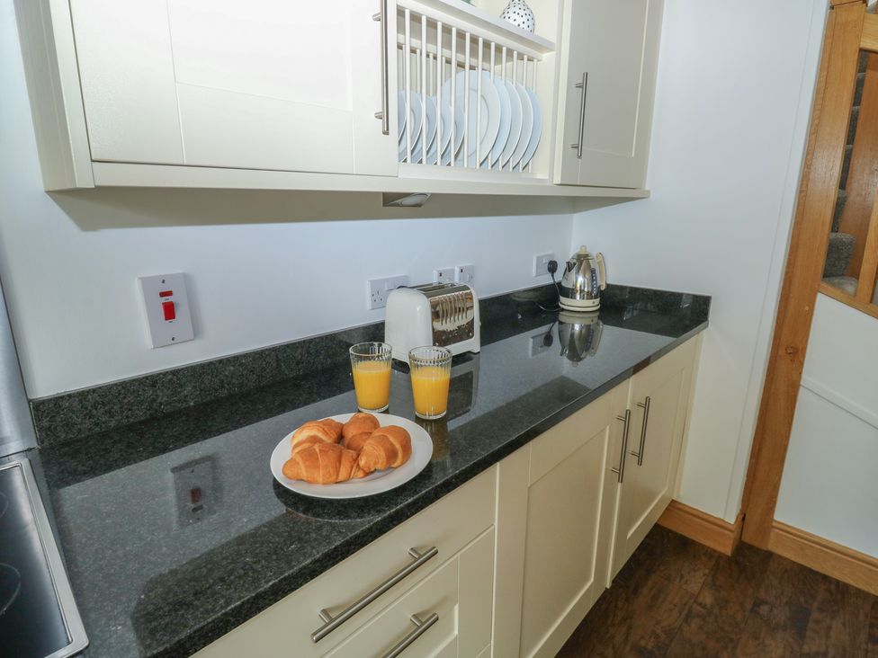 A kitchen with a countertop featuring a kettle, toaster, plates, croissants, and orange juice at 2 Court Cottage in Dartmouth