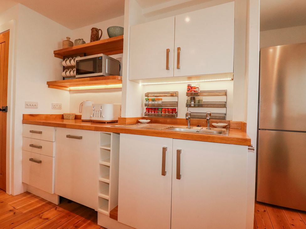 A kitchen with a microwave, sink, and shelves at Logan Barn in Poldue near Camelford