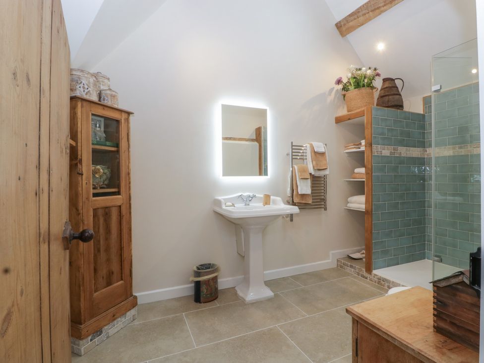 A bathroom with sink, shower, and wooden storage at Cottage - 1 bedroom in Broadway
