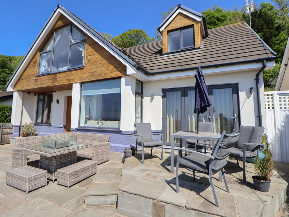 An outdoor patio area with chairs tables and umbrella outside a house with large windows at Buzzards View in Dyserth