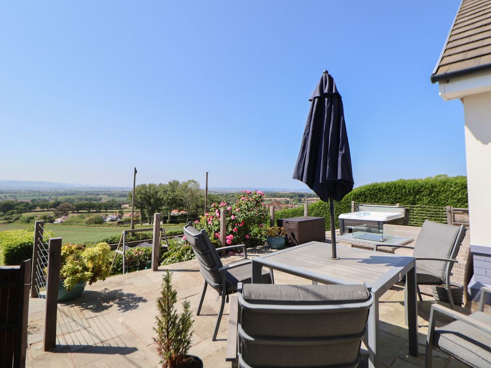 An outdoor patio with chairs table and umbrella overlooking fields and trees at Buzzards View in Dyserth