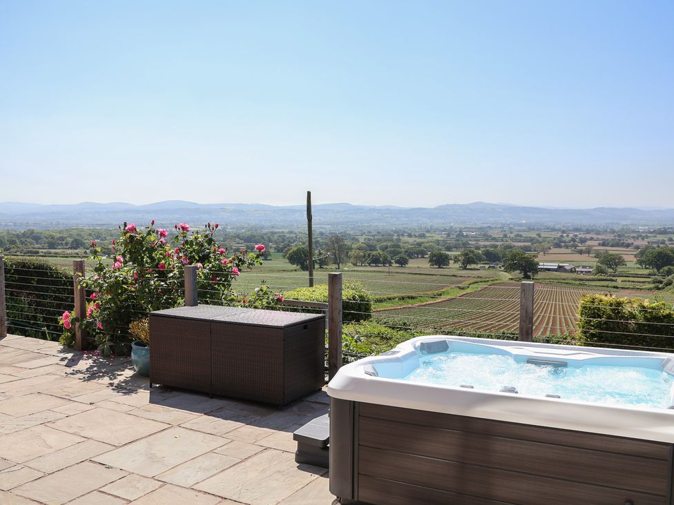 An outdoor patio with a hot tub a storage box and flowers overlooking fields and hills at Buzzards View in Dyserth