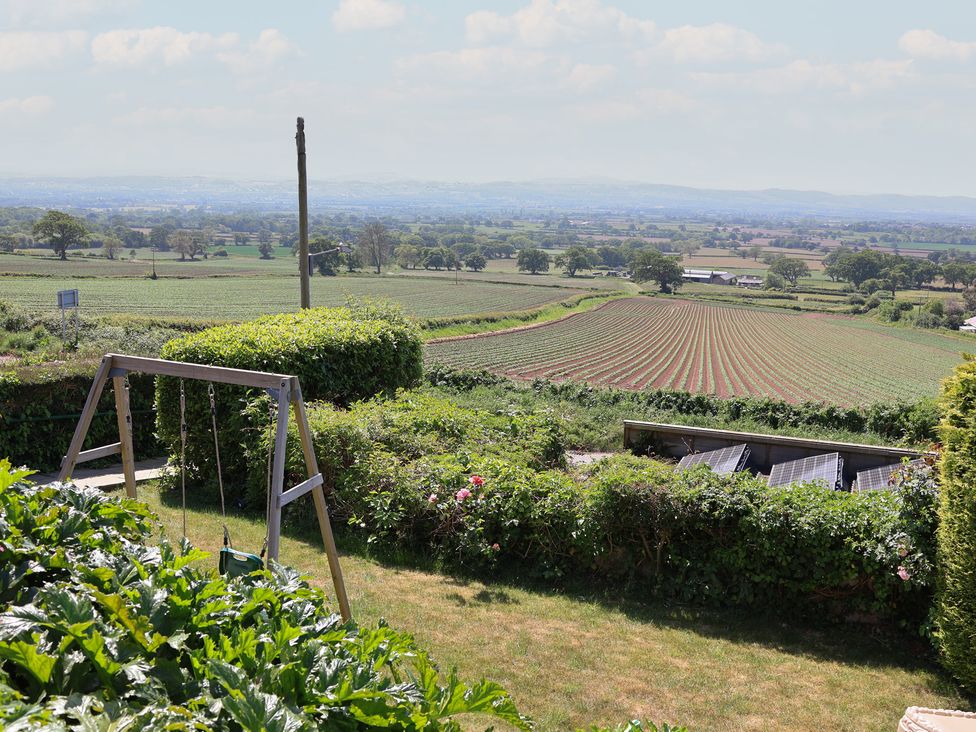 A garden with a wooden swing set and a view of farmland and solar panels at Buzzards View in Dyserth