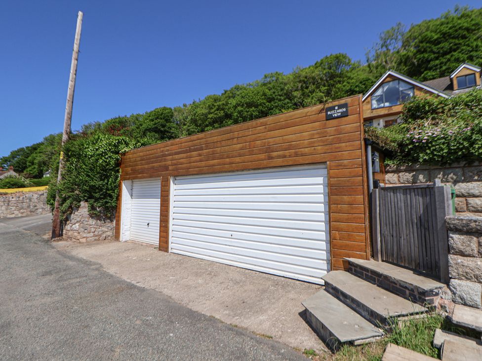 A double garage with white doors and wooden paneling next to stone steps and a wooden gate at Buzzards View in Dyserth