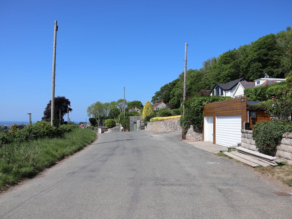 A paved road with garages and houses on the right and grass with utility poles on the left at Buzzards View in Dyserth
