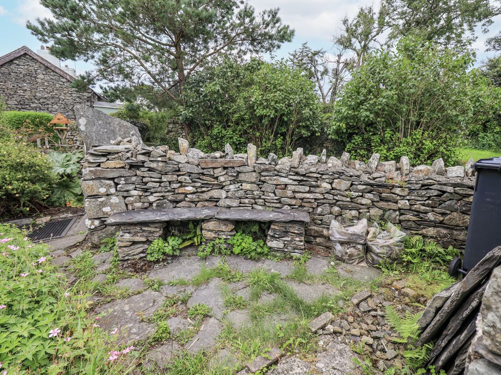 A garden area with a stone wall and wooden bench at Old Cottage in Oxen Park near Ulverston