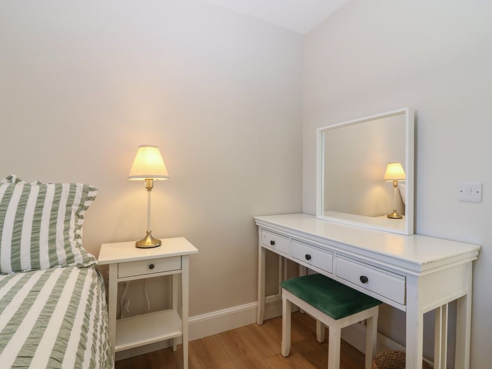 A bedroom with a bed, lamp, nightstand, vanity table, and chair at No 4 - 3 bed in Haddington