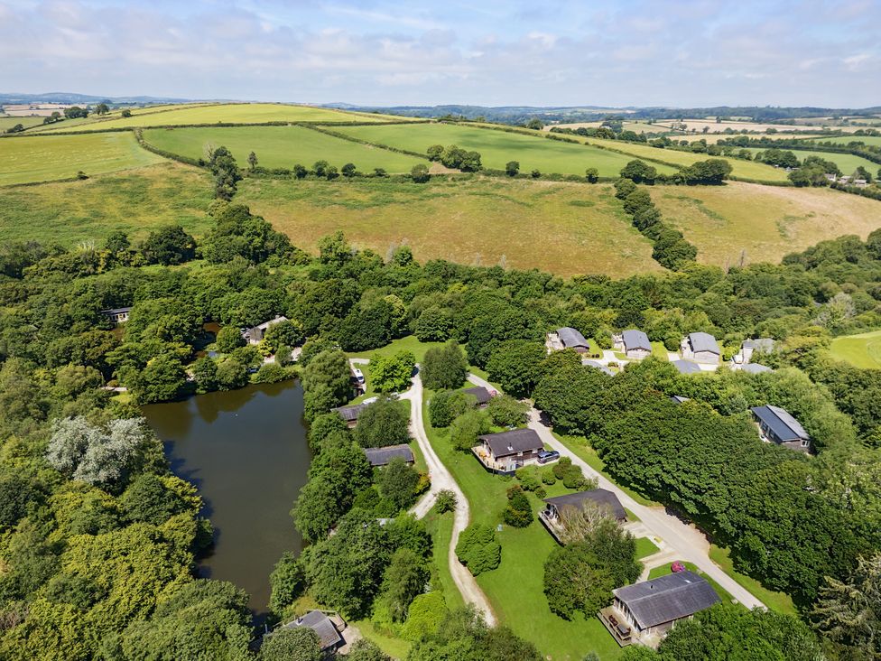 An aerial view of houses near a lake and trees at 3 Hedgerows in Lanreath