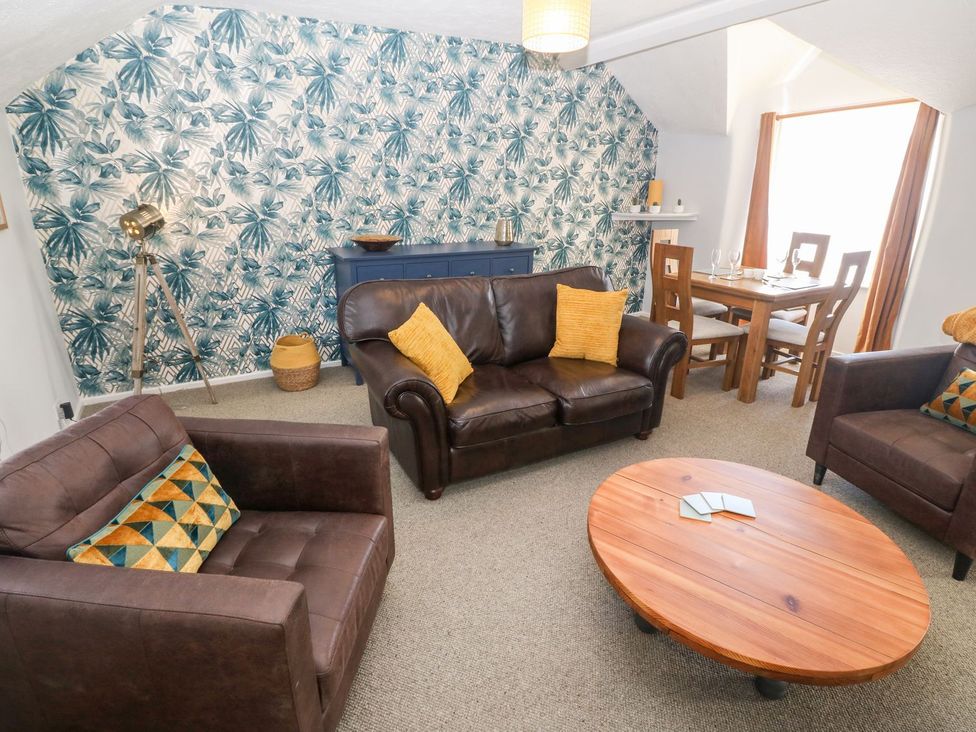 A living room with brown leather sofas yellow cushions a wooden coffee table and a dining table at Medical Hall in Cemaes Bay