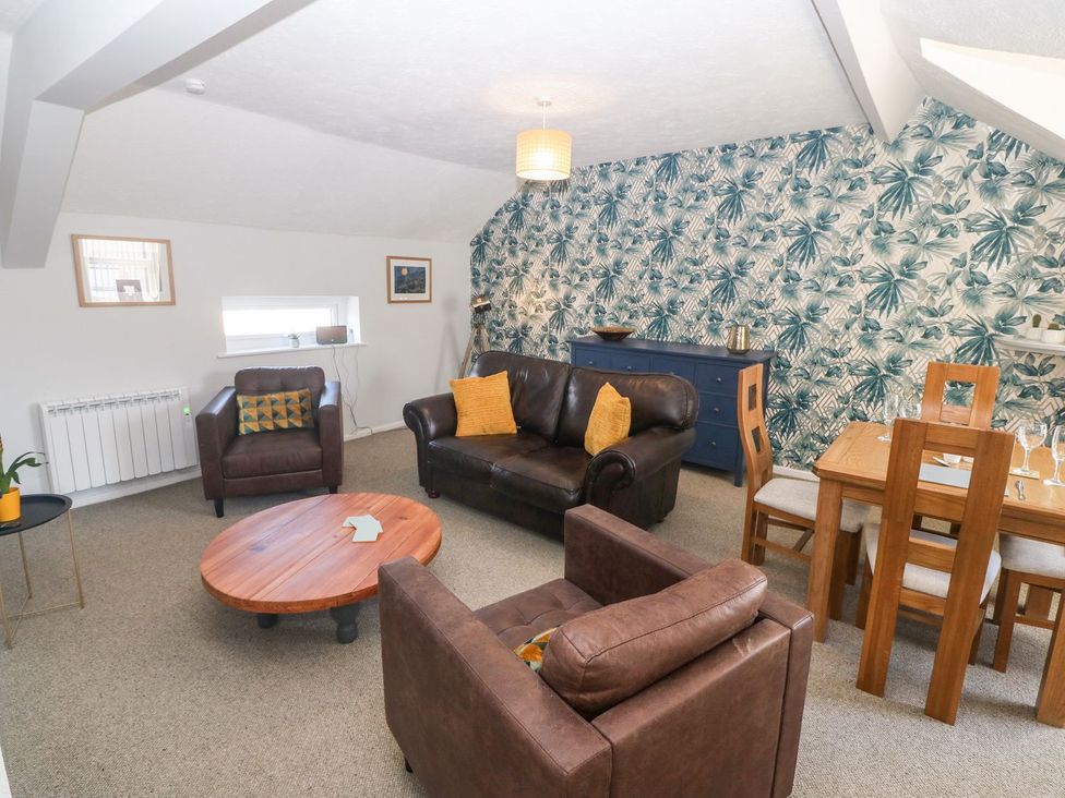 A living room with brown leather sofas wooden coffee table blue sideboard and dining table with chairs at Medical Hall in Cemaes Bay