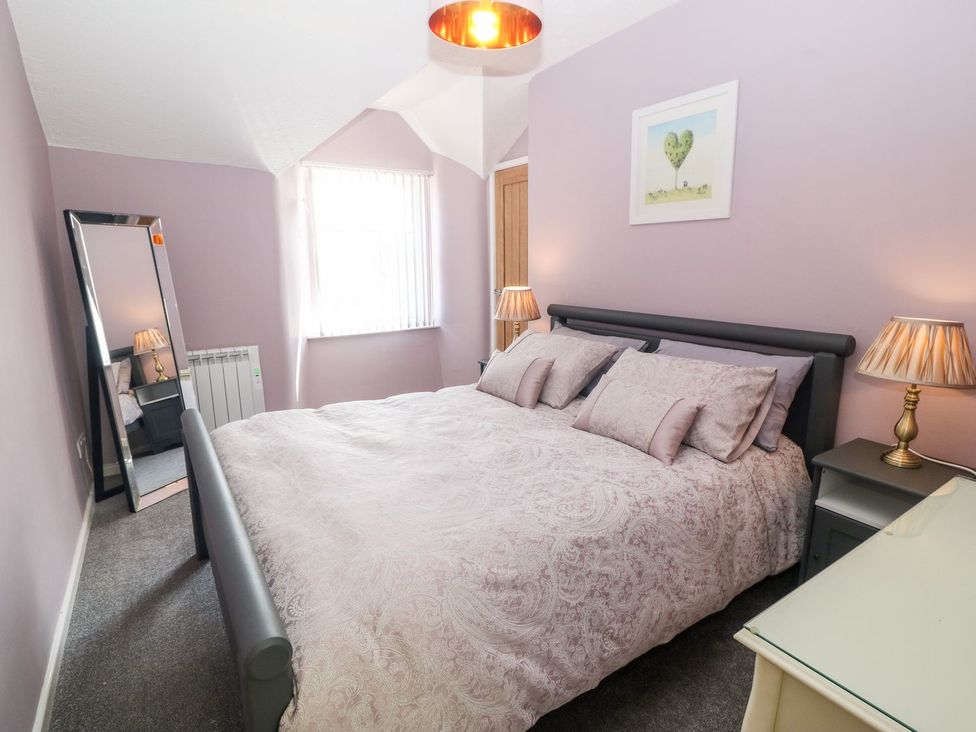 A bedroom with a double bed linens bedside tables lamps a tall mirror and a window at Medical Hall in Cemaes Bay