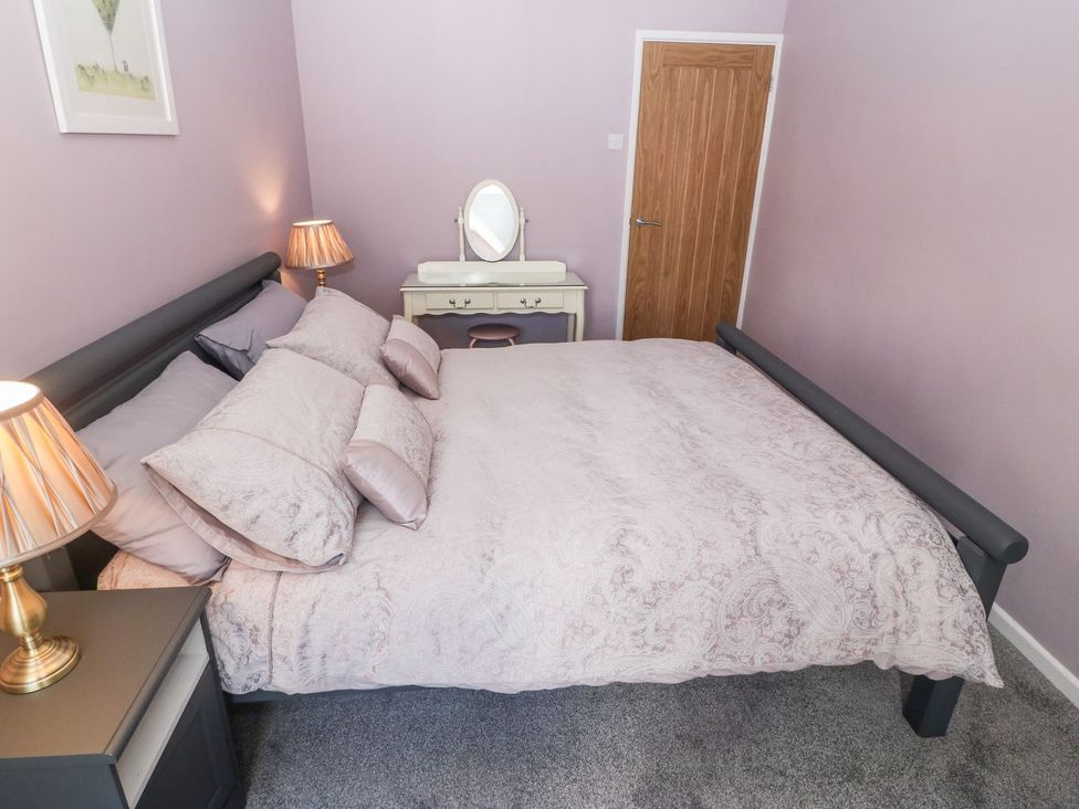 A bedroom with a bed with patterned bedding bedside tables with lamps a dressing table and a wooden door at Medical Hall in Cemaes Bay