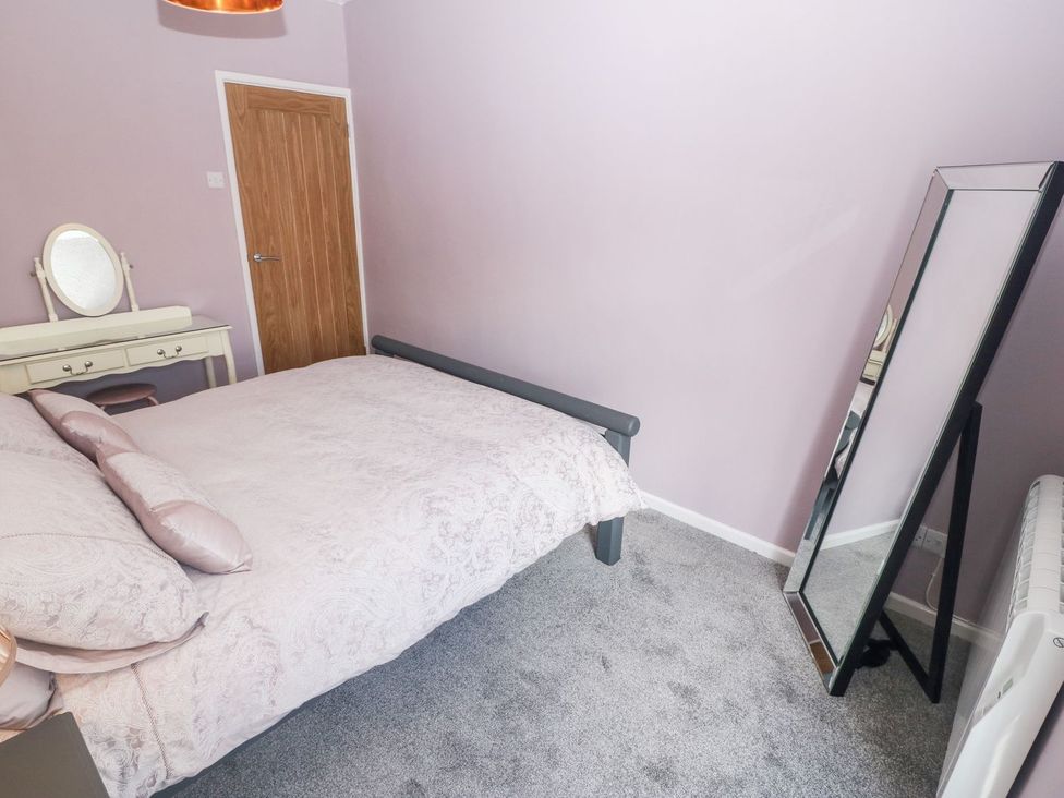 A bedroom with a bed, a dressing table with a mirror, a full-length mirror, a wooden door, and a heater at Medical Hall in Cemaes Bay