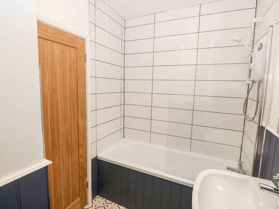 A bathroom with a bathtub and shower unit next to a wooden door at Medical Hall in Cemaes Bay