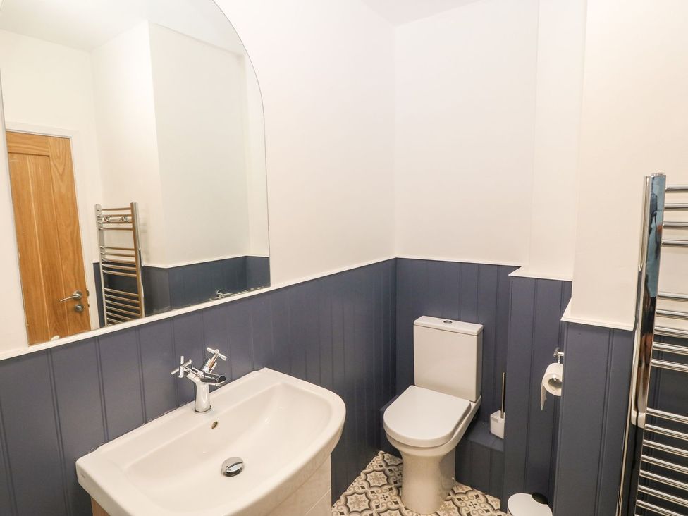 A bathroom with a white sink and chrome faucet a white toilet blue paneled walls patterned floor tiles and a wall-mounted mirror at Medical Hall in Cemaes Bay