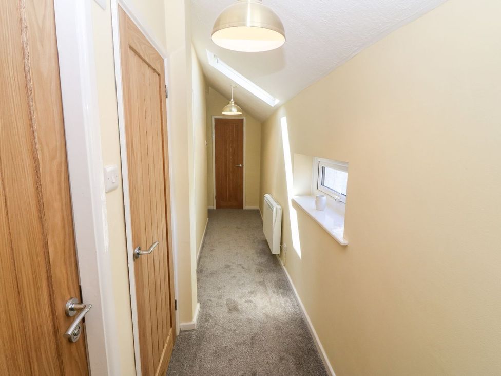 A hallway with three wooden doors beige walls gray carpet skylight window and radiator at Medical Hall in Cemaes Bay