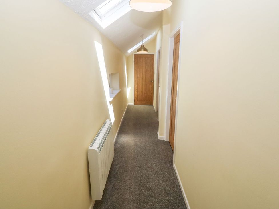 A narrow hallway with beige walls two wooden doors and a skylight window at Medical Hall in Cemaes Bay