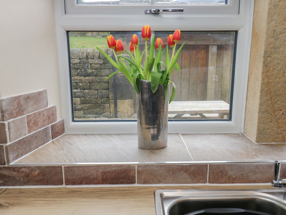 A kitchen with a vase of tulips on the countertop at Moss Cottage in Cragg Vale