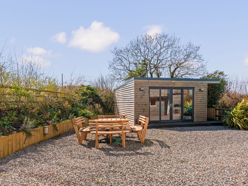 A garden with a wooden seating area and a shed at Capton Snug near Dartmouth
