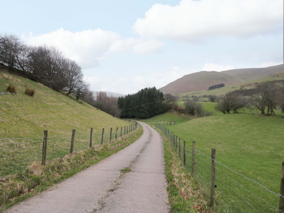 A road bordered by fences and grass with trees and hills at New Barn Conversion Sedbergh