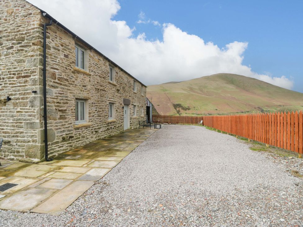 An outdoor view of a stone building with a fenced area and mountains at High Birks Barn Cautley near Sedbergh