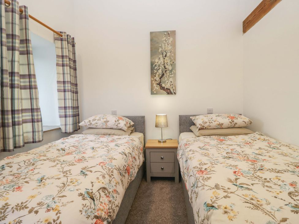 A bedroom with two beds and a lamp on a bedside table at High Birks Barn in Cautley near Sedbergh