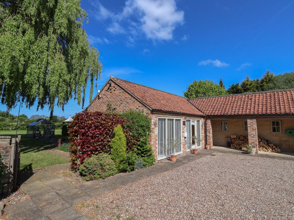 A brick house with tiled roof and large windows surrounded by plants and a gravel driveway at Providence Court Near Easingwold