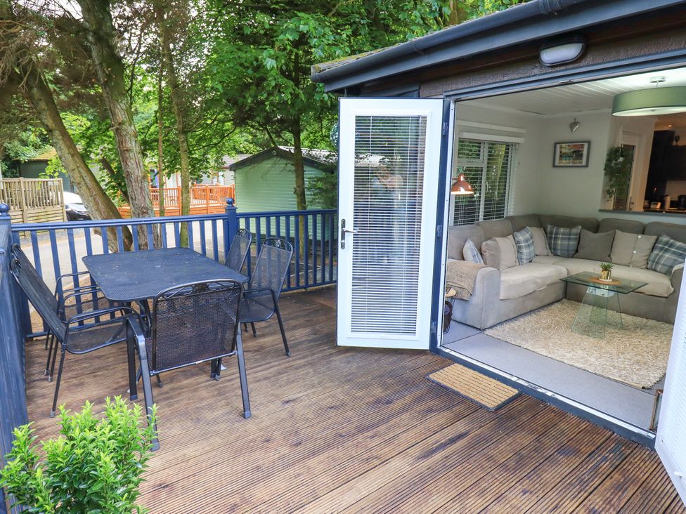 An outdoor deck with a table and chairs overlooking a living area at Evermore Lodge 48 Calgarth Park, White Cross Bay, Windermere