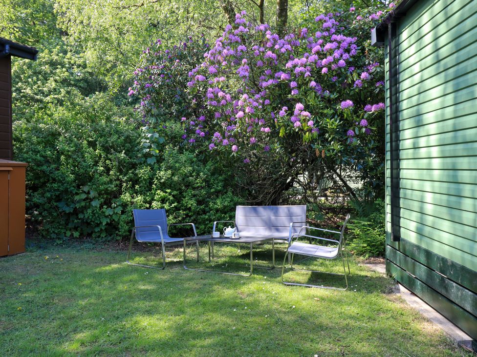 A garden with chairs and a table near a flowering bush at Evermore Lodge, 48 Calgarth Park, White Cross Bay, Windermere