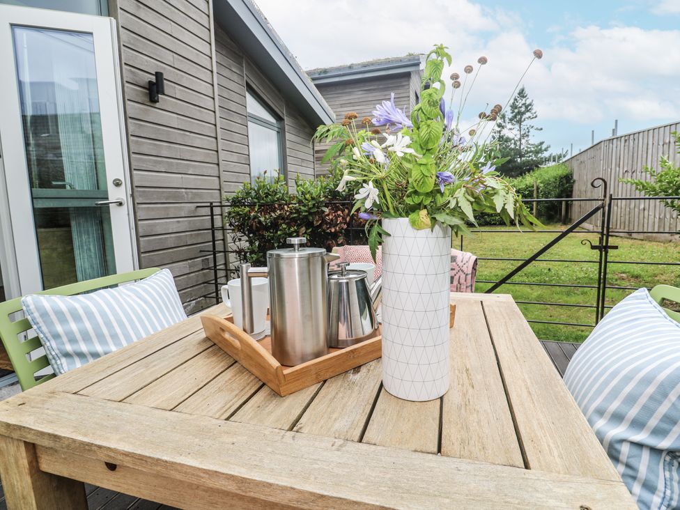 An outdoor table with a vase of flowers and coffee pot at Una, Lodge 70 in Carbis Bay