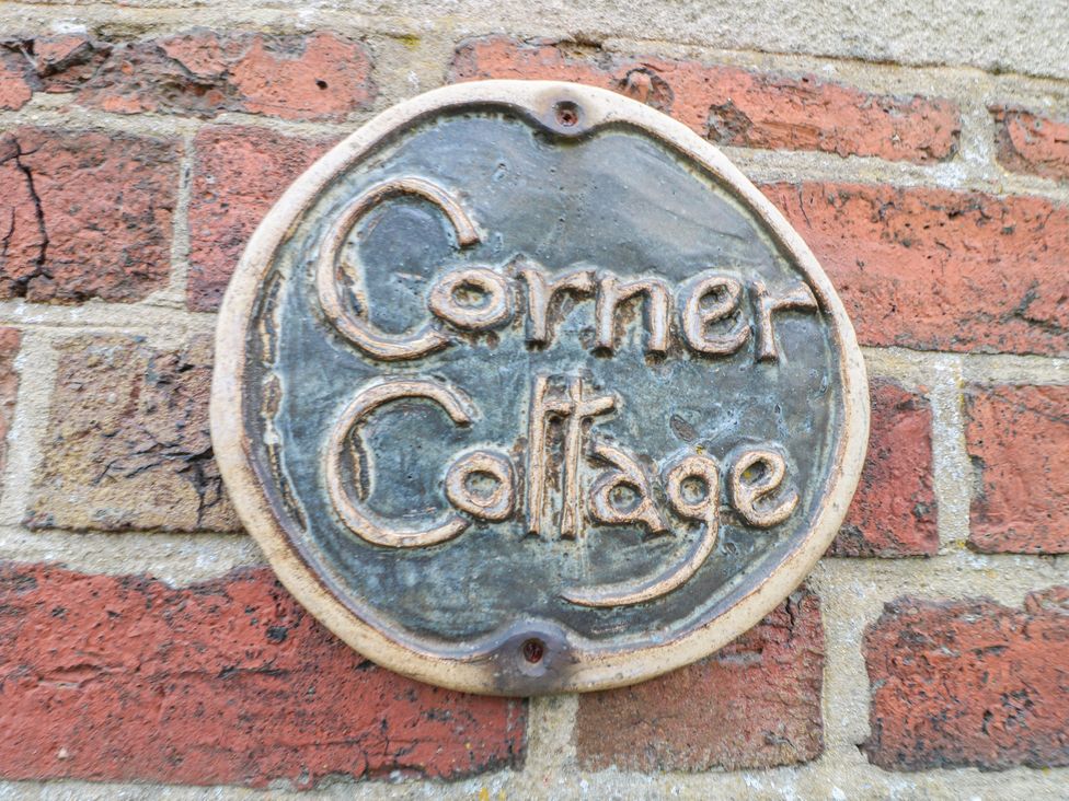 A ceramic sign with the words Corner Cottage on a brick wall at Corner Cottage in Ashbourne