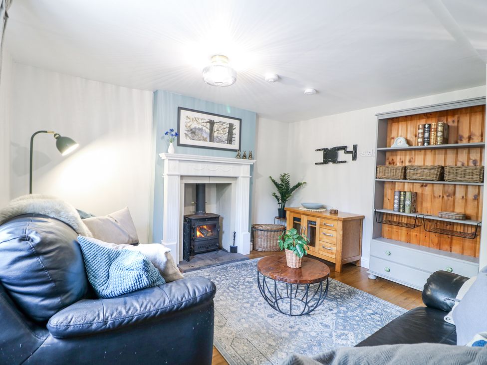 A living room with two black leather sofas a fireplace and a wooden coffee table at Corner Cottage in Ashbourne