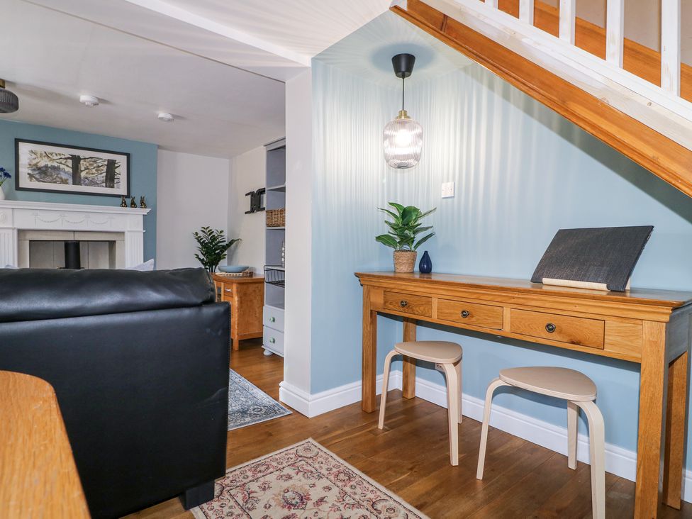A wooden desk with two stools under stairs next to a living room with a fireplace at Corner Cottage in Ashbourne
