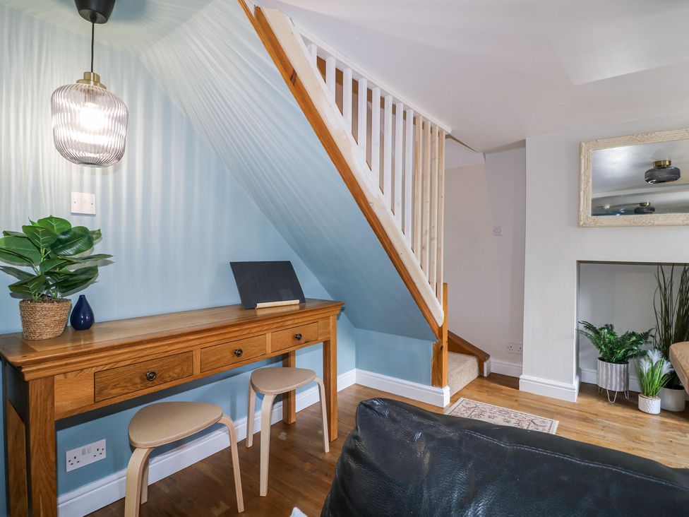 A wooden table with drawers and two stools under stairs with plants and a mirror at Corner Cottage in Ashbourne