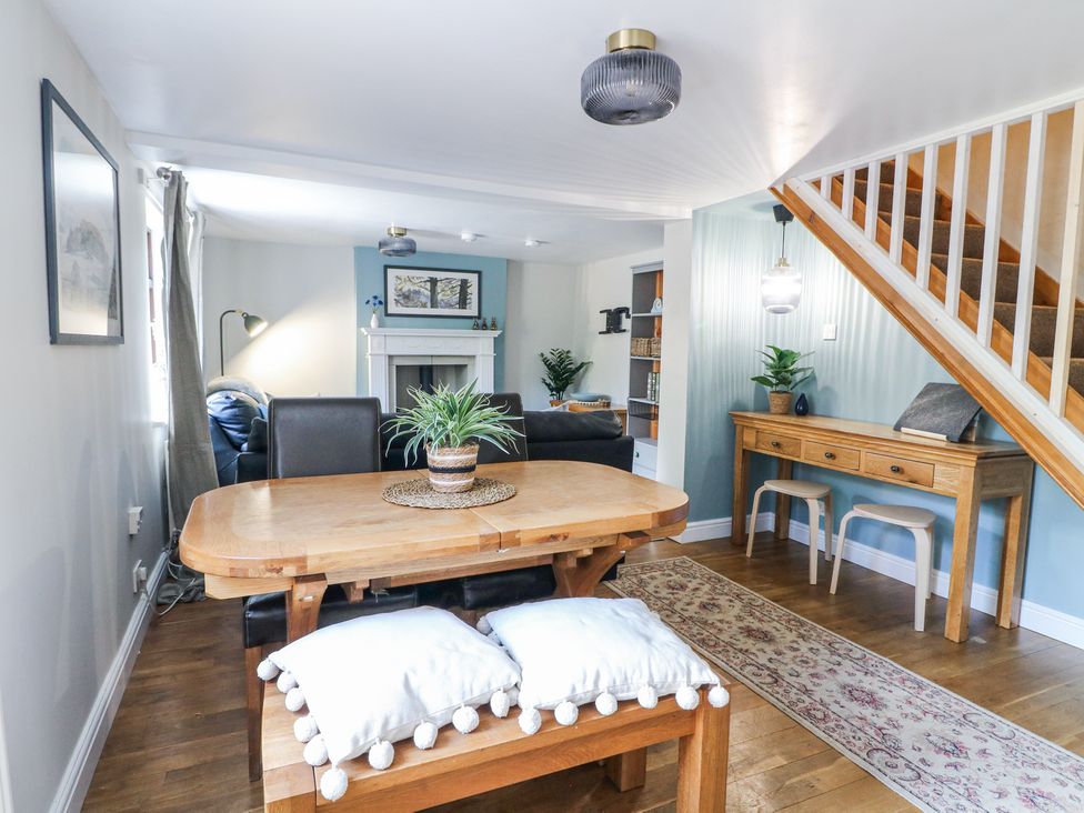 A dining table with chairs and bench and a living area with a fireplace and sofas at Corner Cottage in Ashbourne