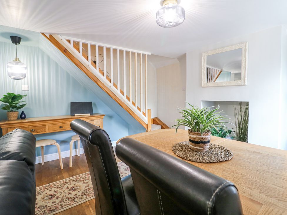 A dining area with a wooden table and black chairs near a staircase and a wooden console table at Corner Cottage in Ashbourne