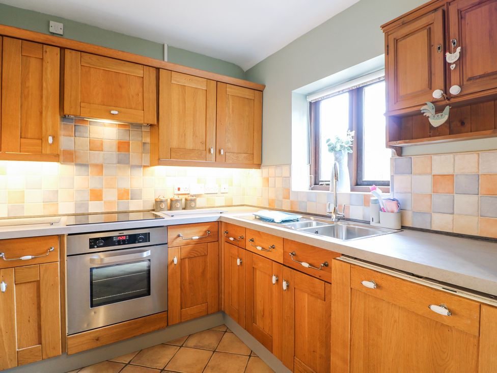 A kitchen with wooden cabinets a built in oven a double sink and a window at Corner Cottage in Ashbourne