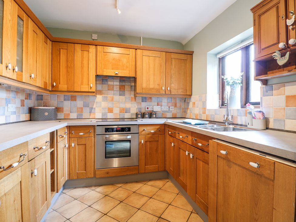 A kitchen with wooden cabinets a built in oven and a sink under a window at Corner Cottage in Ashbourne