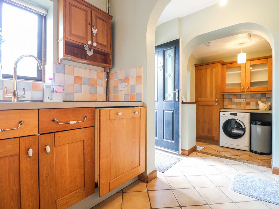 A kitchen area with wooden cabinets a washing machine and an open door at Corner Cottage in Ashbourne