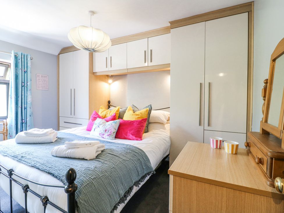 A bedroom with a bed, colorful pillows, folded towels, built-in wardrobes, a wooden dresser with a mirror and two striped cups at Corner Cottage in Ashbourne