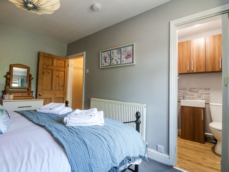 A bedroom with a bed and stacked towels next to a bathroom with wooden cabinets at Corner Cottage in Ashbourne
